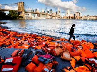 A woman in New York walks past hundreds of refugee life jackets collected from the beaches of Greece Sept. 16, 2016. The U.S. bishops in a pastoral reflection released March 22 called all Catholics to do what each of them can "to accompany migrants and refugees who seek a better life in the United States." (CNS photo/Justin Lane, EPA) See BISHOPS-REFLECTION-MIGRANTS-REFUGEES March 22, 2017.