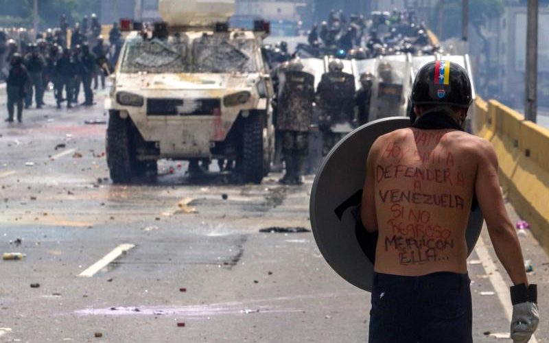 A protester faces the National Guard during clashes May 10 in Caracas, Venezuela. The motto on his back reads: "Mom, today I went out to defend Venezuela. If I do not come back, I went with her." Latin American bishops will discuss the evolving political crisis in Venezuela during a four-day long assembly in El Salvador. (CNS photo/Miguel Guitierrez, EPA) See CELAM-VENEZUELA May 10, 2017.
