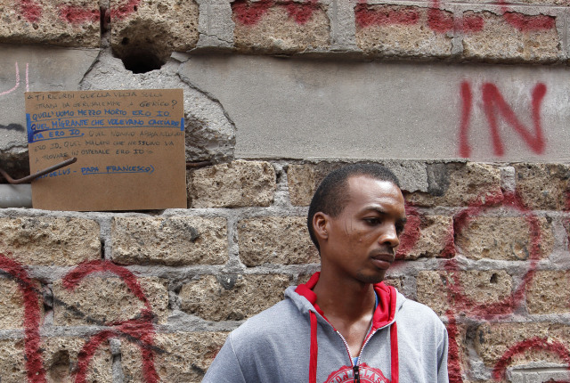 Josef, who said he arrived from Sudan 10 days earlier, holds clothes he received from volunteers as he stands on a street in Rome July 14. In the background is a quote from Pope Francis about helping refugees. Several refugees said they were planning to head north to countries such as France and Germany. (CNS photo/Paul Haring) See VATICAN-MOBILE-MEDICAL July 14, 2016.