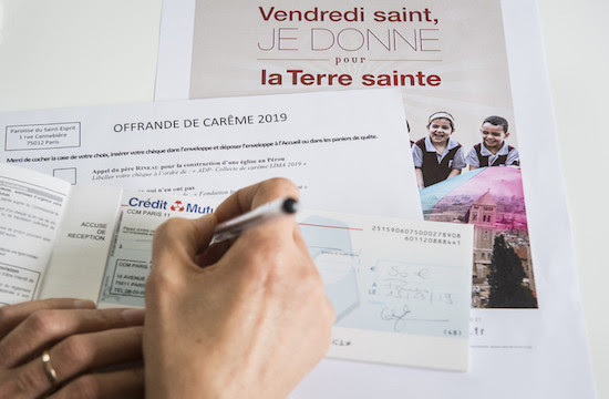 Một người phụ nữ viết một tấm séc để quyên góp trong Mùa Chay, ở Pháp. (Ảnh của CORINNE SIMON / CIRIC)