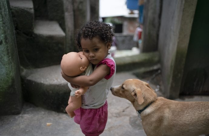 Một cô gái ôm con búp bê của mình trong một con hẻm của khu ổ chuột Rocinha ở Rio de Janeiro, Brazil, Thứ Ba, ngày 24 tháng 3 năm 2020. Những con hẻm hẹp ở favela lớn nhất của Brazil làm giảm luồng không khí xung quanh các ngôi nhà chật cứng và khu dân cư nghèo, không có nước thải thích hợp, có tỷ lệ mắc bệnh lao cao. Các nhà chức trách lo ngại rằng COVID-19 có thể dễ dàng lây lan ở khu ổ chuột ở Rio. (Ảnh: Leo Correa / AP)