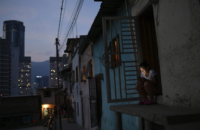 Một người phụ nữ nhìn vào chiếc điện thoại thông minh của mình bên ngoài ngôi nhà của mình ở khu phố San Agustin ở Venezuela, Venezuela, Chủ nhật, ngày 17 tháng 5 năm 2020. Tổng thống Nicolas Maduro đang thư giãn các biện pháp kiểm dịch vào cuối tuần bằng cách cho phép trẻ em và người lớn tuổi ra khỏi nhà của họ Vài giờ mỗi ngày. (Tín dụng: Matias Delacroix / AP.)