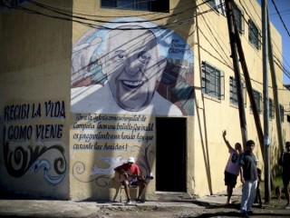 Một người đàn ông chơi guitar bên dưới bức tranh tường của Giáo hoàng Francis trong một cuộc khóa cửa do chính phủ ra lệnh để ngăn chặn sự lây lan của coronavirus mới ở Buenos Aires, Argentina, Thứ Tư, ngày 29 tháng 4 năm 2020. (Tín dụng: Natacha Pisarenko./AP)