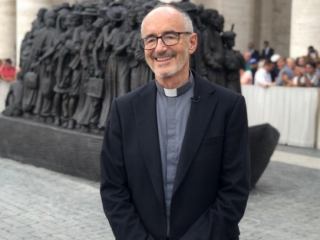 Hồng y Michael Czerny trước tác phẩm điêu khắc 'Angels Unawares' của những người di cư tại Quảng trường Thánh Peter ở Vatican. (Ảnh: Wikipedia)