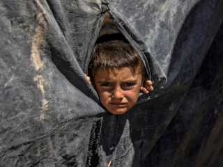 Một cậu bé nhìn ra từ một căn lều tại trại al-Hol do người Kurd điều hành ở tỉnh al-Hasakeh ở đông bắc Syria, nơi giam giữ các gia đình của các chiến binh nước ngoài của Nhà nước Hồi giáo (Ảnh: AFP)