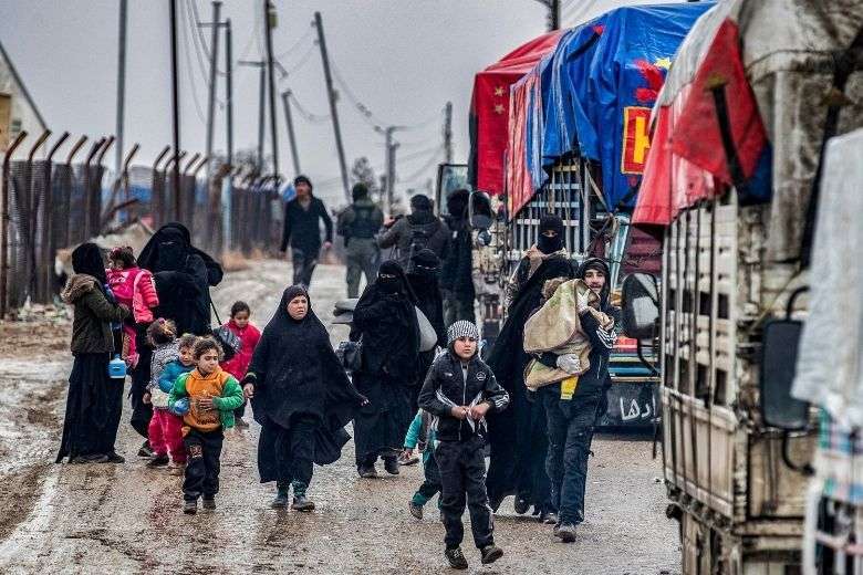 Một người đàn ông bế một đứa trẻ khi anh ta đi cùng phụ nữ và trẻ em khác trước một thành viên của cơ quan an ninh nội bộ người Kurd Syria được gọi là Asayish khi họ tiến về phía xe tải trong quá trình giải phóng những người bị nghi ngờ có liên quan đến các chiến binh Nhà nước Hồi giáo khỏi lực lượng người Kurd điều hành Trại al-Hol ở đông bắc Syria, vào ngày 19 tháng 1. (Ảnh: AFP)