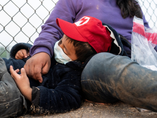 Sau khi vượt sông Rio Grande từ Mexico vào Hoa Kỳ để xin tị nạn, một đứa trẻ di cư 4 tuổi đang mẹ ngủ trên mặt đất trong khi họ chờ được Đội tuần tra biên giới chở đến ở La Joya, Texas, ngày 8/4/2021 (Ảnh: CNS / Go Nakamura, Reuters)