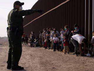 Một nhân viên Tuần tra Biên giới ở Penitas, Texas, hướng dẫn những người di cư xin tị nạn vào ngày 17 tháng 3 năm 2021, khi họ xếp hàng dọc theo bức tường biên giới sau khi băng qua Rio Grande. Cơ quan Thực thi Di trú và Hải quan báo cáo hơn 12.000 trường hợp nhiễm coronavirus trong các trung tâm giam giữ (Ảnh: Adrees Latif / Reuters)