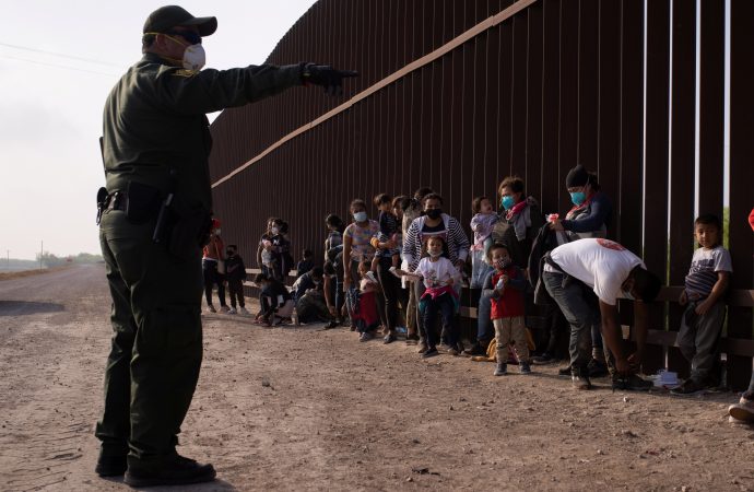 Một nhân viên Tuần tra Biên giới ở Penitas, Texas, hướng dẫn những người di cư xin tị nạn vào ngày 17 tháng 3 năm 2021, khi họ xếp hàng dọc theo bức tường biên giới sau khi băng qua Rio Grande. Cơ quan Thực thi Di trú và Hải quan báo cáo hơn 12.000 trường hợp nhiễm coronavirus trong các trung tâm giam giữ (Ảnh: Adrees Latif / Reuters)