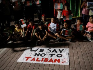 Trẻ em ngồi trước biểu ngữ "Chúng tôi nói không với Taliban" khi người di cư Afghanistan biểu tình trên đảo Lesbos, Hy Lạp, ngày 16 tháng 8 năm 2021, chống lại sự tiếp quản của Taliban ở Afghanistan. (Credit: Elias Marcou / Reuters qua CNS.)