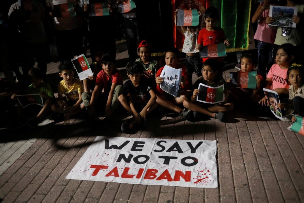 Trẻ em ngồi trước biểu ngữ "Chúng tôi nói không với Taliban" khi người di cư Afghanistan biểu tình trên đảo Lesbos, Hy Lạp, ngày 16 tháng 8 năm 2021, chống lại sự tiếp quản của Taliban ở Afghanistan. (Credit: Elias Marcou / Reuters qua CNS.)
