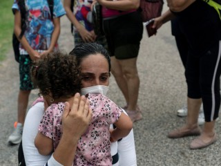 Một người mẹ nhập cư từ Venezuela ôm lấy đứa con của mình khi chúng chờ được Đội tuần tra biên giới vận chuyển sau khi băng qua Rio Grande vào Del Rio, Texas, ngày 27 tháng 5 năm 2021 (Ảnn: Go Nakamura / Reuters qua CNS)