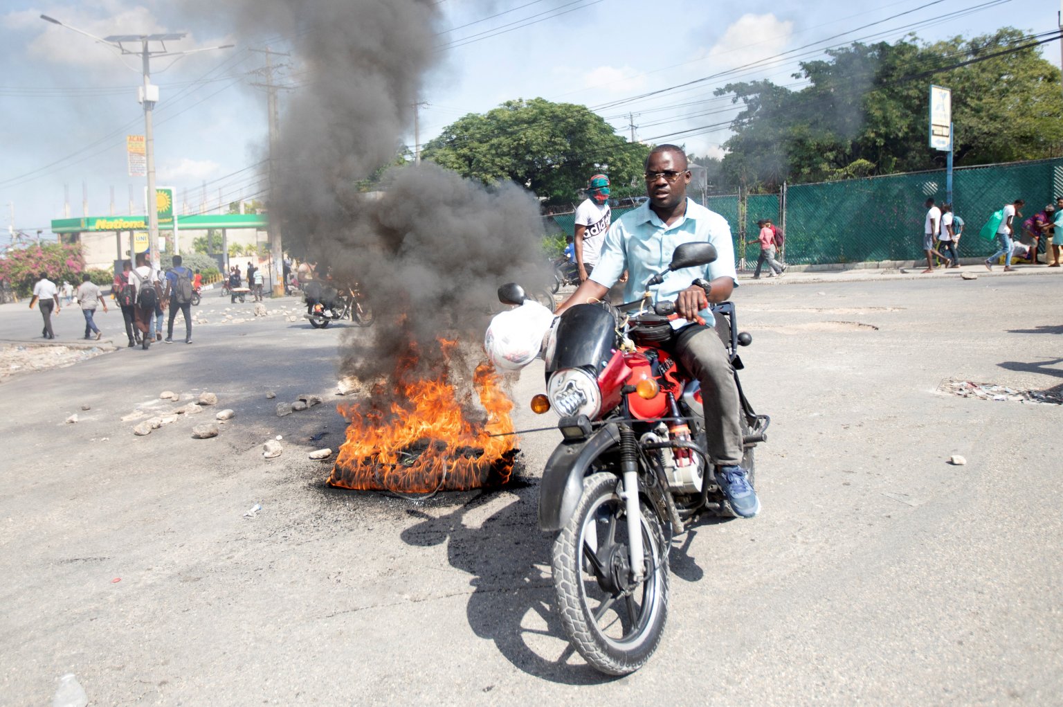 Một người đàn ông ở Port-au-Prince, Haiti, lái chiếc xe máy của mình vượt qua chướng ngại vật đang bốc cháy vào ngày 20 tháng 10 năm 2021, khi những người biểu tình tham gia phản đối giá cao và tình trạng thiếu nhiên liệu. (Tín dụng: Ralph Tedy Erol / Reuters qua CNS)