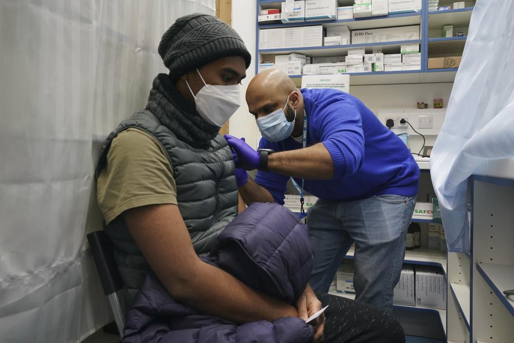 Y tá Salak Ali, phải, thực hiện tiêm nhắc lại vắc xin 'Jingle Jab' Covid cho một bệnh nhân, tại Good Health Pharmacy, bắc London, Thứ Bảy, ngày 25 tháng 12 năm 2021. Hàng nghìn người trên khắp nước Anh đã dành vài phút trong Ngày Giáng sinh để Xếp hàng dưới bầu trời mùa đông chì để được tiêm vắc xin chống lại COVID-19 vì biến thể omicron thúc đẩy sự gia tăng các ca nhiễm trùng trên khắp đất nước. (Nguồn: Gareth Fuller / PA qua AP)