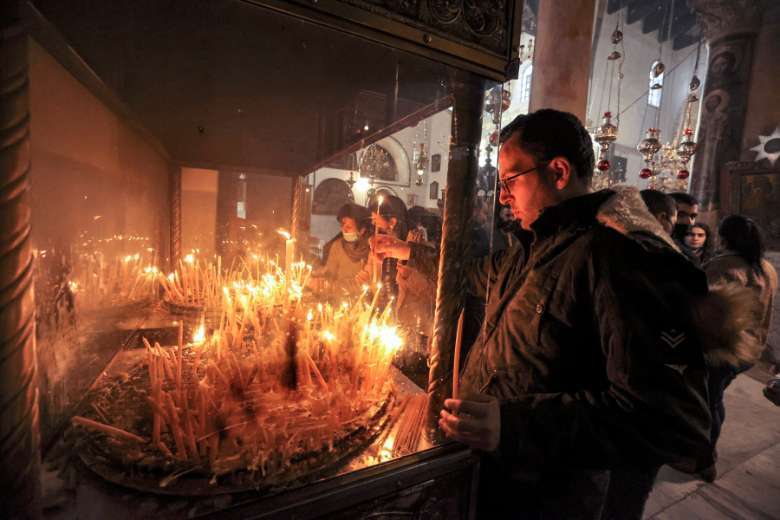 Milad Ayyad, một tín đồ Cơ đốc giáo chính thống Hy Lạp gốc Palestine từ Gaza, thắp nến tại Vương cung thánh đường Hy Lạp ở Nhà thờ Chúa giáng sinh, nơi truyền thống sinh ra của Chúa, ở thành phố Bethlehem trong Kinh thánh ở Bờ Tây bị chiếm đóng vào ngày 26 tháng 12 năm 2021 (Ảnh : AFP)