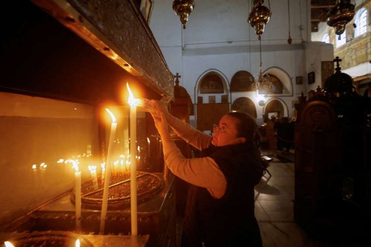 Một người phụ nữ thắp nến trước buổi lễ bắt đầu mùa Giáng sinh tại Nhà thờ Chúa Giáng Sinh ở Bethlehem, Bờ Tây, ngày 26 tháng 11 năm 2022. Trong thông điệp Giáng sinh của họ, các Thượng phụ và những người đứng đầu các Giáo hội tại Thánh Địa đã so sánh đau khổ của những người tị nạn với đau khổ của Thánh Gia (Ảnh: CNS /Mussa Qawasma, Reuters) 