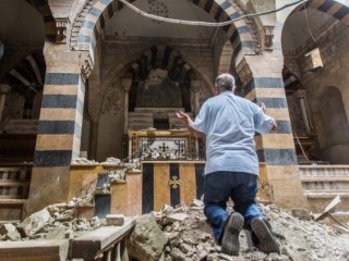 Một người đàn ông quỳ trước một nhà thờ bị phá hủy