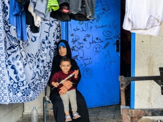 Một người phụ nữ ngồi bên đống quần áo đang phơi với một đứa trẻ bên ngoài một lớp học tại một trường học do Cơ quan Cứu trợ và Việc làm của Liên Hợp Quốc dành cho Người tị nạn Palestine ở Cận Đông (UNRWA) ở Rafah, phía nam Dải Gaza vào ngày 14 tháng 11 năm 2023, nơi những người Palestine di dời đã trú ẩn trong bối cảnh các cuộc giao tranh đang diễn ra giữa Israel và nhóm chiến binh Palestine Hamas (Ảnh: SAID KHATIB / AFP qua Getty Images)