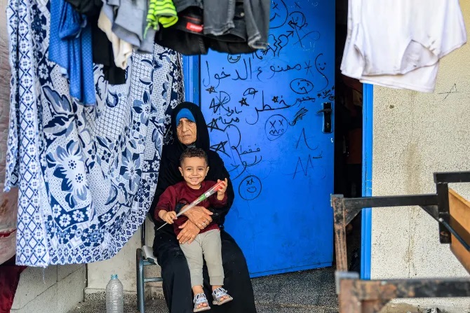 Một người phụ nữ ngồi bên đống quần áo đang phơi với một đứa trẻ bên ngoài một lớp học tại một trường học do Cơ quan Cứu trợ và Việc làm của Liên Hợp Quốc dành cho Người tị nạn Palestine ở Cận Đông (UNRWA) ở Rafah, phía nam Dải Gaza vào ngày 14 tháng 11 năm 2023, nơi những người Palestine di dời đã trú ẩn trong bối cảnh các cuộc giao tranh đang diễn ra giữa Israel và nhóm chiến binh Palestine Hamas (Ảnh: SAID KHATIB / AFP qua Getty Images)