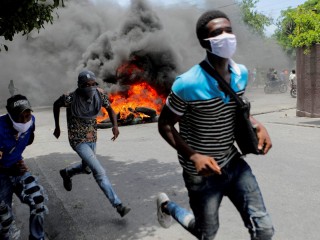 Những người đàn ông chạy cạnh những chiếc lốp xe đang cháy trong cuộc biểu tình ngày 14 tháng 8 năm 2023 yêu cầu chấm dứt bạo lực băng đảng ở Port-au-Prince, Haiti. Vatican News đưa tin vào ngày 19 tháng 1 năm 2024, rằng những người có vũ trang ở Port-au-Prince đã chiếm một chiếc xe buýt và bắt cóc ít nhất sáu nữ tu và những người khác trên xe buýt. Các tay súng được cho là thành viên băng đảng (Ảnh: OSV News/Ralph Tedy Erol, Reuters)