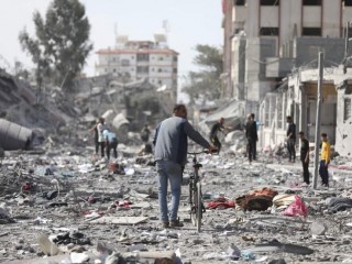 Người dân Palestine đi ngang qua các tòa nhà bị phá hủy trong cuộc ném bom của Israel vào al-Zahra, ngoại ô thành phố Gaza (Ảnh: Ali Mahmoud/AP)