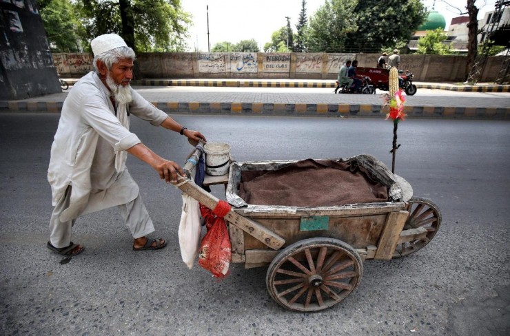 Một người bán hàng rong lớn tuổi đẩy chiếc xe gỗ của mình trên lề đường ở Peshawar, Pakistan (Ảnh: ANSA)